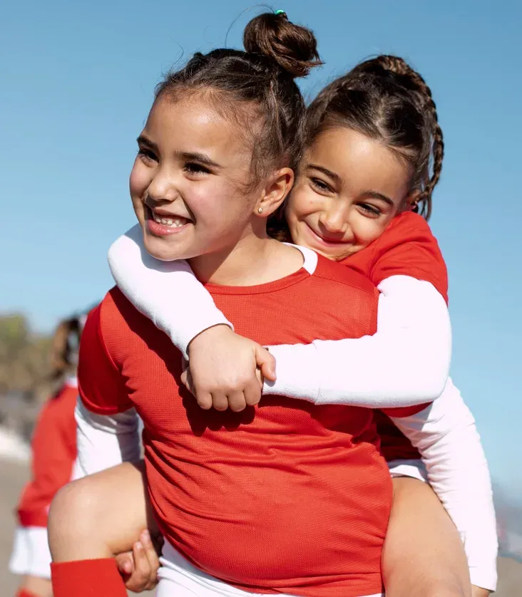 Duas meninas de uniforme vermelho se abraçando
